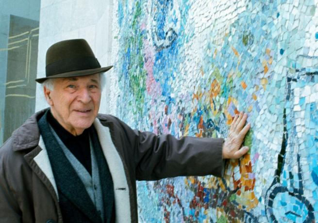 Şapkalı sanatçı Marc Chagall elini mavi mozaik tasarımlarla duvara bastırıyor.