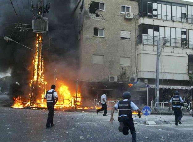 İsrail polisi, İsrail'in kuzeyindeki Nahariya kasabasında 13 Temmuz 2006'da Hizbullah roketlerinin bir voleybolu tarafından vurulduktan hemen sonra yanan bir elektrik direği olay yerine koştu ve bina hasar gördü.