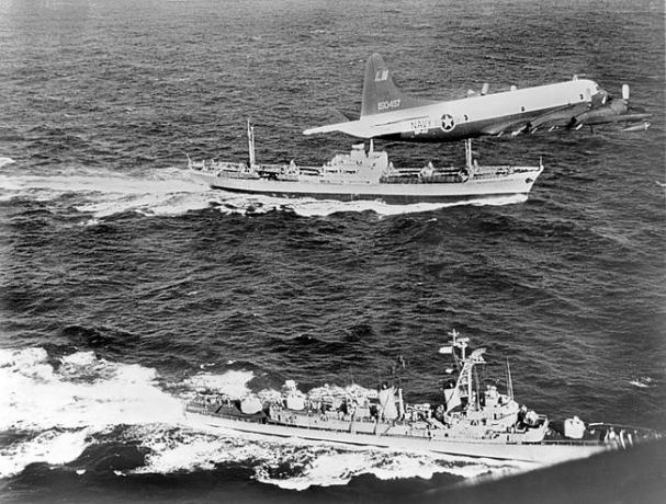 Sovyet yük gemisi Anosov, arkada, 1962 Küba Füze Krizi sırasında Küba'dan ayrılırken bir Donanma uçağı ve destroyer USS Barry tarafından eşlik ediliyor.