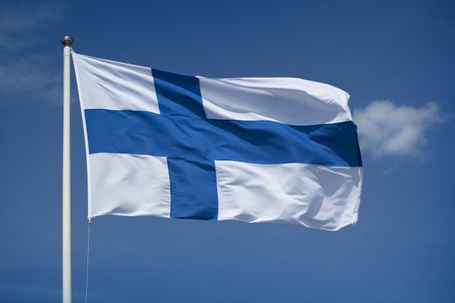 Arka planda mavi gökyüzü olan Finlandiya bayrağını kaldırdı