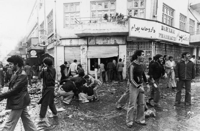 4 Kasım 1978 Tahran'daki bir isyandan sonra diğerleri bir dükkânı yağmalarken, insanlar yaralı etrafında toplandı